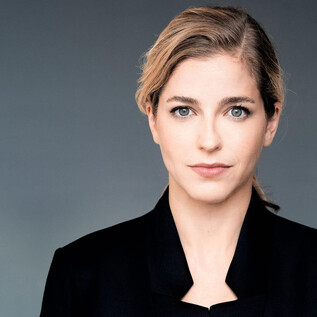 A person with blonde hair and a serious expression looks directly at the camera. They are wearing a black jacket against a neutral background. | © Mathias Bothor