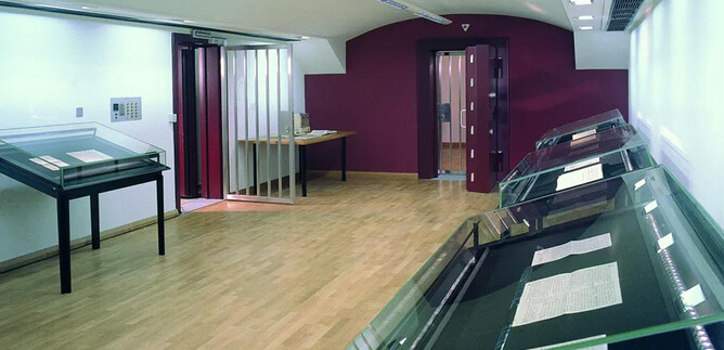 A modern exhibition room with wooden floors and bright walls. Glass display pieces are placed along the walls. | © ISM
