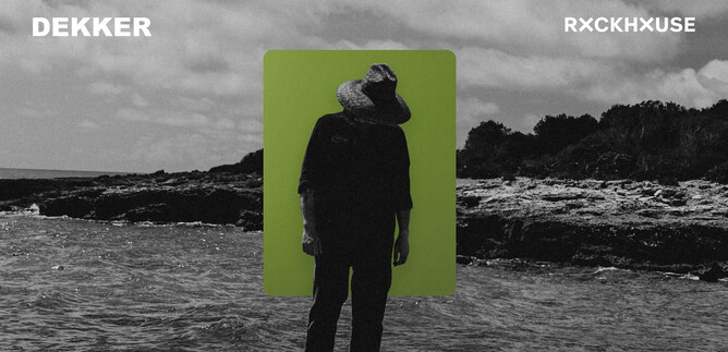 A man stands on the beach with a hat and has his head lowered. In the background, there are waves and a cloudy sky. | © James Keane