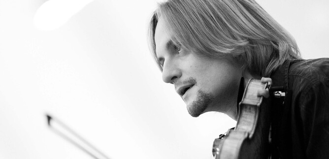 A musician is playing the violin and has long hair. The recording is in black and white. | © DomRadio