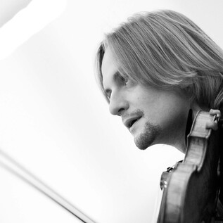 A musician is playing the violin and has long hair. The recording is in black and white. | © DomRadio