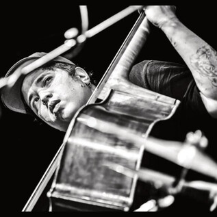 A musician passionately plays a cello on stage. He is wearing a cap and has visible tattoos. | © Jazzit