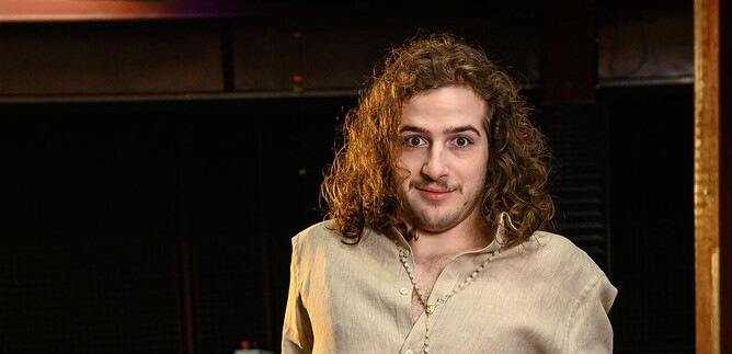 A young man with curly hair is standing in a room. He is wearing a simple top and looking directly at the camera. | © SLT / Tobias Witzgall
