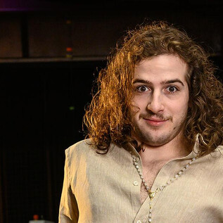 A young man with curly hair is standing in a room. He is wearing a simple top and looking directly at the camera. | © SLT / Tobias Witzgall