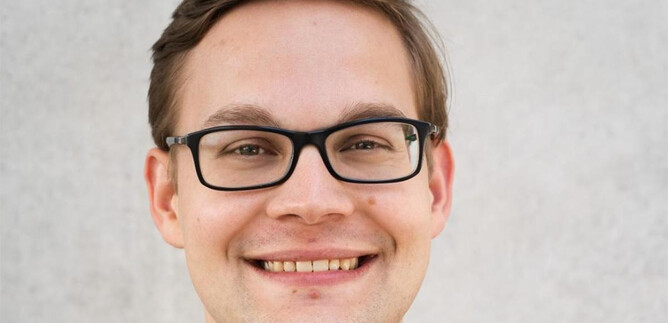 A young man with glasses is smiling at the camera. The background is bright and neutral. | © www.salzburger-dom.at