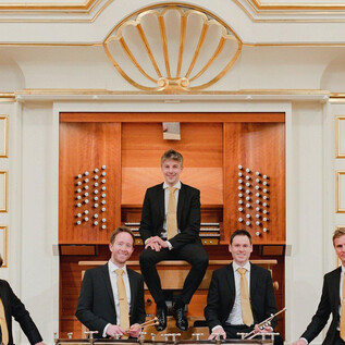 A group of five musicians stands and sits in front of an organ. They wear elegant suits and smile at the camera. | © Sophie Baubin
