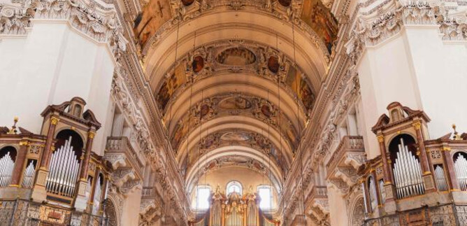 A magnificent church with high ceilings and ornate frescoes. Impressive organs can be seen on the walls. | © Dom zu Salzburg
