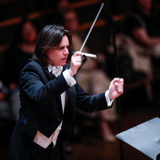 A conductor leads an orchestra on stage. The audience in the background is attentive and enjoying the performance. | © Salzburger Kulturvereinigung_Pixell