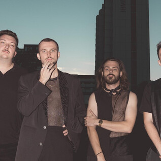 A group of four men stands in front of an urban background. The scene conveys a modern and stylish ambiance. | © Arne Müseler