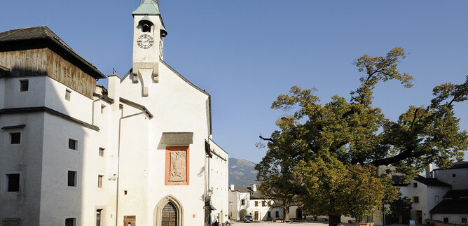 Un endroit calme avec une église blanche et un grand arbre. Le ciel est clair et bleu, ce qui crée une atmosphère paisible. | © Salzburger Burgen und Schlösser