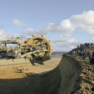 Three traffic signs stand in a snowy landscape. The atmosphere is gray and foggy, with a quiet stream in the background. | © Nolting