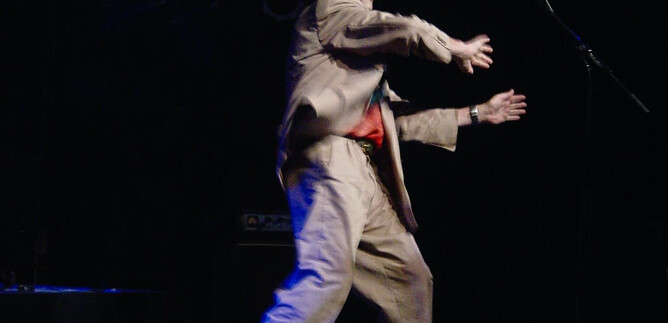 An artist on stage is performing. He is wearing a suit and a hat while colorful lights are shining. | © Roswitha Pross