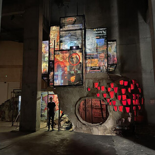 A modern art space with large-scale projections on the walls and a sculptural structure. In the background, a person can be seen exploring the atmosphere. | © Museum der Moderne Salzburg_wildbild, Rohrer