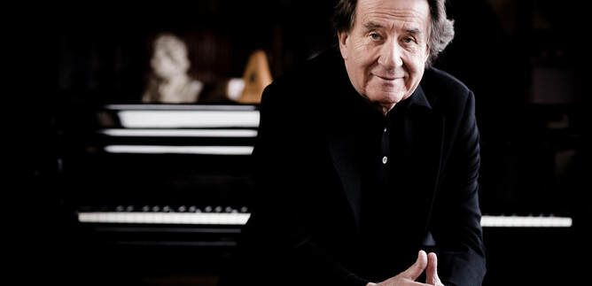 A smiling man sits in front of a piano. The background is dark and creates a creative atmosphere. | © Marco Borggreve