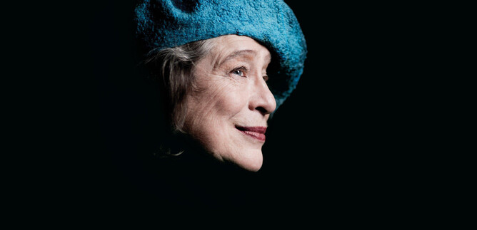 An older woman with a blue hat is smiling. The image has a dark background and shows her head from the side. | © Marco Borggreve