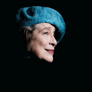 An older woman with a blue hat is smiling. The image has a dark background and shows her head from the side. | © Marco Borggreve