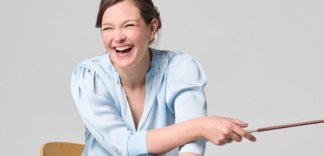 A smiling woman is sitting on a chair and holding a pointer. She is wearing a light blue shirt and appears happy and excited. | © Kaupo Kikkas