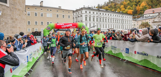 A running event with multiple participants, who set off under a colorful start arch. The spectators stand on the sidelines and watch the event. | © Sportograf