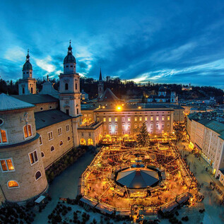 A picturesque city view at dusk with illuminated buildings and a festive Christmas market in the center. The atmosphere is cozy and inviting. | © Tourismus Salzburg GmbH