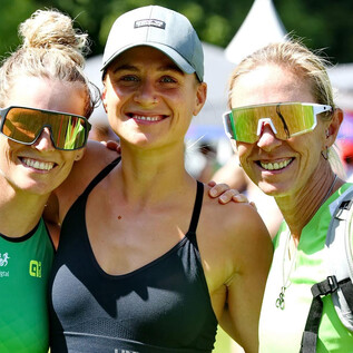 Three athletic women are smiling together at the camera. They are wearing sunglasses and are dressed in sporty clothing. | © Sepp Kühnhold