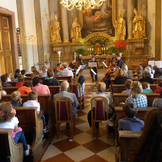A concert in a festive space with many listeners. The musicians are performing on stage in front of a golden backdrop.