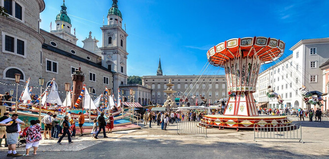 A bustling square with a carousel and festive attractions. Surrounded by historic buildings and a backdrop of blue sky. | © Tourismus Salzburg / G. Breitegger