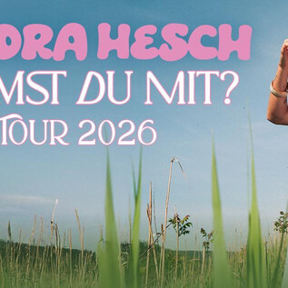 A young woman stands in a green field with a bright sky. She is wearing a casual outfit and is smiling warmly at the camera. | © Sebastian Balz