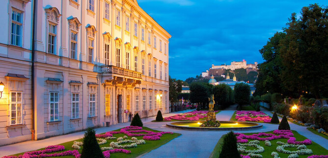 An elegant building with beautiful garden landscapes at dusk. A castle can be seen in the background. | © Salzburger Konzertgesellschaft