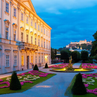 An elegant building with beautiful garden landscapes at dusk. A castle can be seen in the background. | © Salzburger Konzertgesellschaft