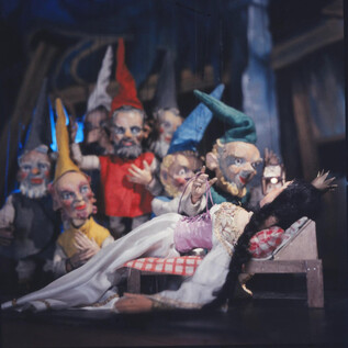 A group of colorful dolls stands around a sleeping figure. The scene looks fairy-tale-like and inviting. | © Salzburger Marionettentheater