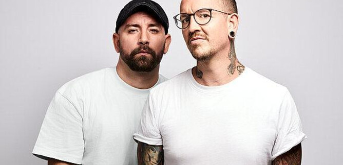 Two men are standing next to each other and looking at the camera. Both have visible tattoos and are wearing casual clothing. | © Barracuda Music GmbH