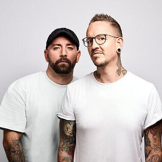 Two men are standing next to each other and looking at the camera. Both have visible tattoos and are wearing casual clothing. | © Barracuda Music GmbH