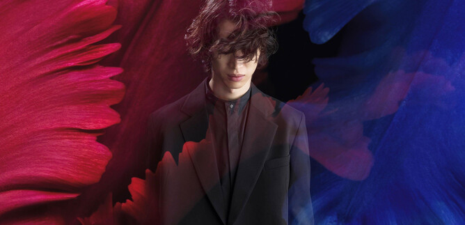 A young man stands in a black suit against a colored background. Red and blue brush strokes surround him, giving the picture an artistic touch. | © RyuyaAmao