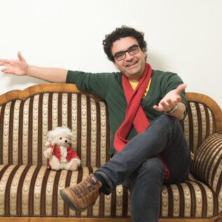 Ein Mann sitzt entspannt auf einer Couch und lächelt freundlich. Neben ihm sitzt ein kleiner Hund, der ebenfalls fröhlich aussieht. | © Wolfgang Lienbacher