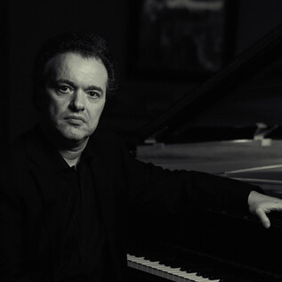 A man is sitting at the piano and looking seriously at the camera. The monochrome shot conveys an elegant and contemplative atmosphere. | © Philip Andrukovich