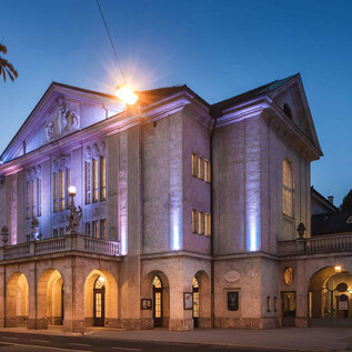 A historic building with impressive architecture, illuminated in soft colors. It is located in an urban setting at dusk. | © Christian Schneider