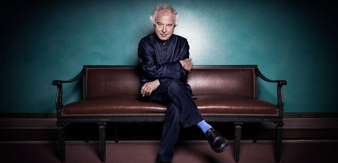 A man is sitting on a bench with an elegant, contemplative expression. The wall in the background is in a deep green tone. | © Nadja_Sjostrom