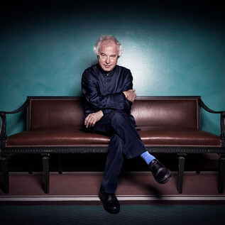 A man is sitting on a bench with an elegant, contemplative expression. The wall in the background is in a deep green tone. | © Nadja_Sjostrom