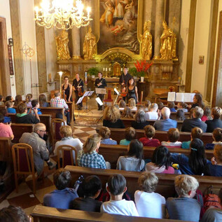 A concert in a church with a large number of listeners. On stage, several musicians are playing their instruments.
