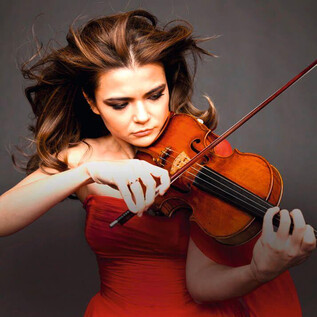 A talented violinist passionately plays her instrument. She is wearing a red dress and has long, flowing hair. | © o.A.