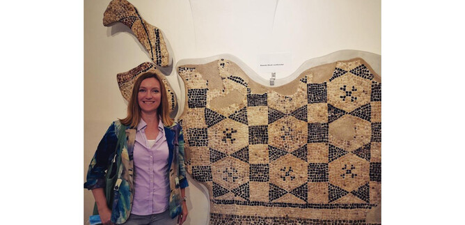 A person stands next to a large, artistically designed wall installation made of various patterns. The installation features a traditional garment and some accessories. | © Sabine Rath