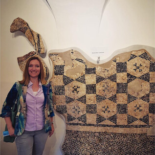 A person stands next to a large, artistically designed wall installation made of various patterns. The installation features a traditional garment and some accessories. | © Sabine Rath