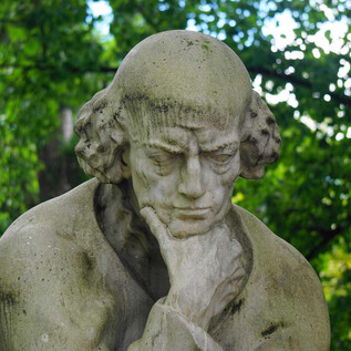 A contemplative statue with a sculpted expression. It stands surrounded by green trees. | © Mag. Christoph Koca