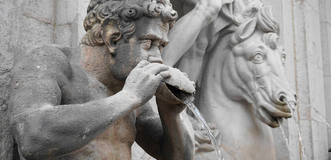 Starobylá socha muže, z jehož nádoby teče voda. V pozadí je vidět kůň s detailně propracovanou hlavou. | © Mag. Christoph Koca