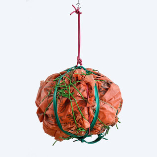 An orange, round-shaped sculpture that is wrapped in green ribbons and hangs from a pink thread. The background is light and neutral. | © The Estate of Stano Filko