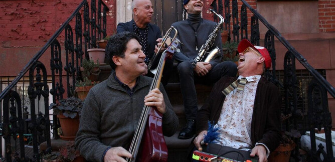 Four musicians are sitting on a staircase and playing different instruments. They are laughing and enjoying the atmosphere. | © Greg Aiello