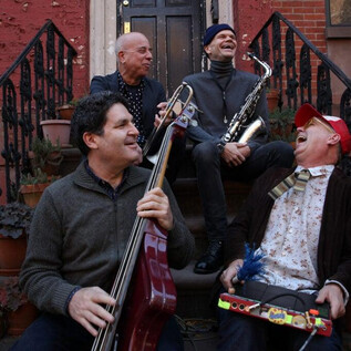 Four musicians are sitting on a staircase and playing different instruments. They are laughing and enjoying the atmosphere. | © Greg Aiello