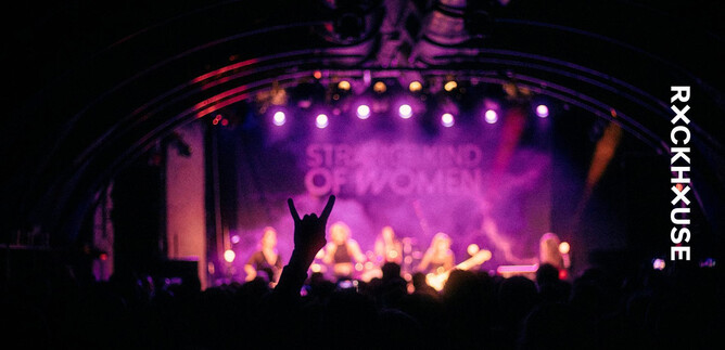 A concert with a band on stage and colorful lights in the background. A fan raises their hand in a sign of excitement. | © Rockhouse Salzburg