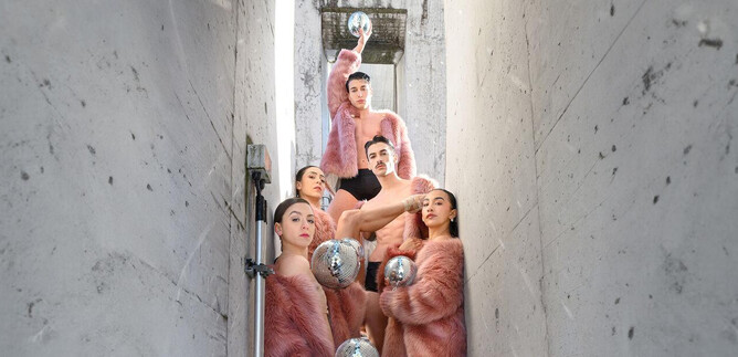 A group of people in pink furs stands in a narrow, gray corridor. They are holding silver objects in their hands and posing for the photo. | © SLT / Christian Krautzberger