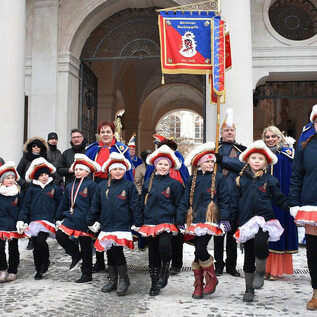 A group of children in traditional costumes stands on a street at an event. In the background, spectators and decorations can be seen. | © 1. Salzburger Faschingsgilde
